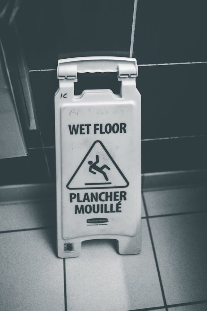 Black and white image of a wet floor sign in a tiled indoor space.